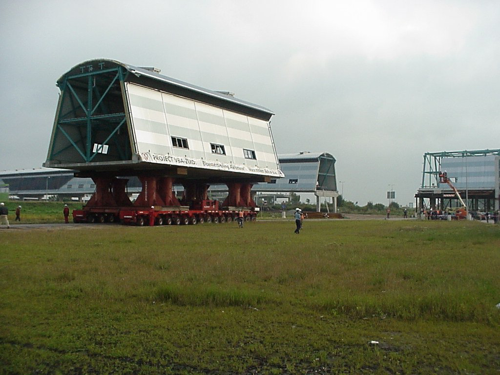 Grote metalen constructies op rode trailers in een grasveld, een bouw- of transportterrein.