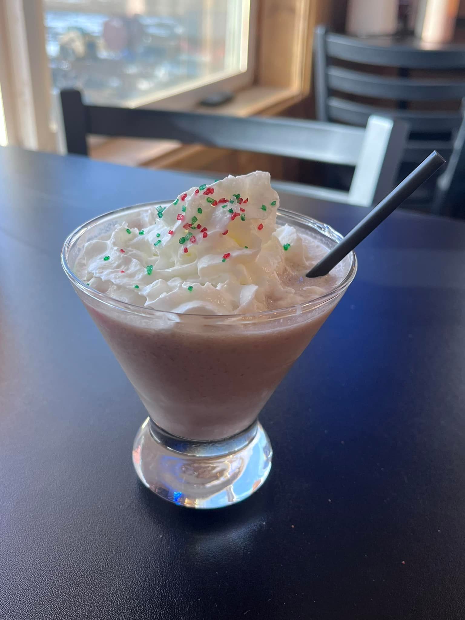 A martini with whipped cream and sprinkles on top is on a table.