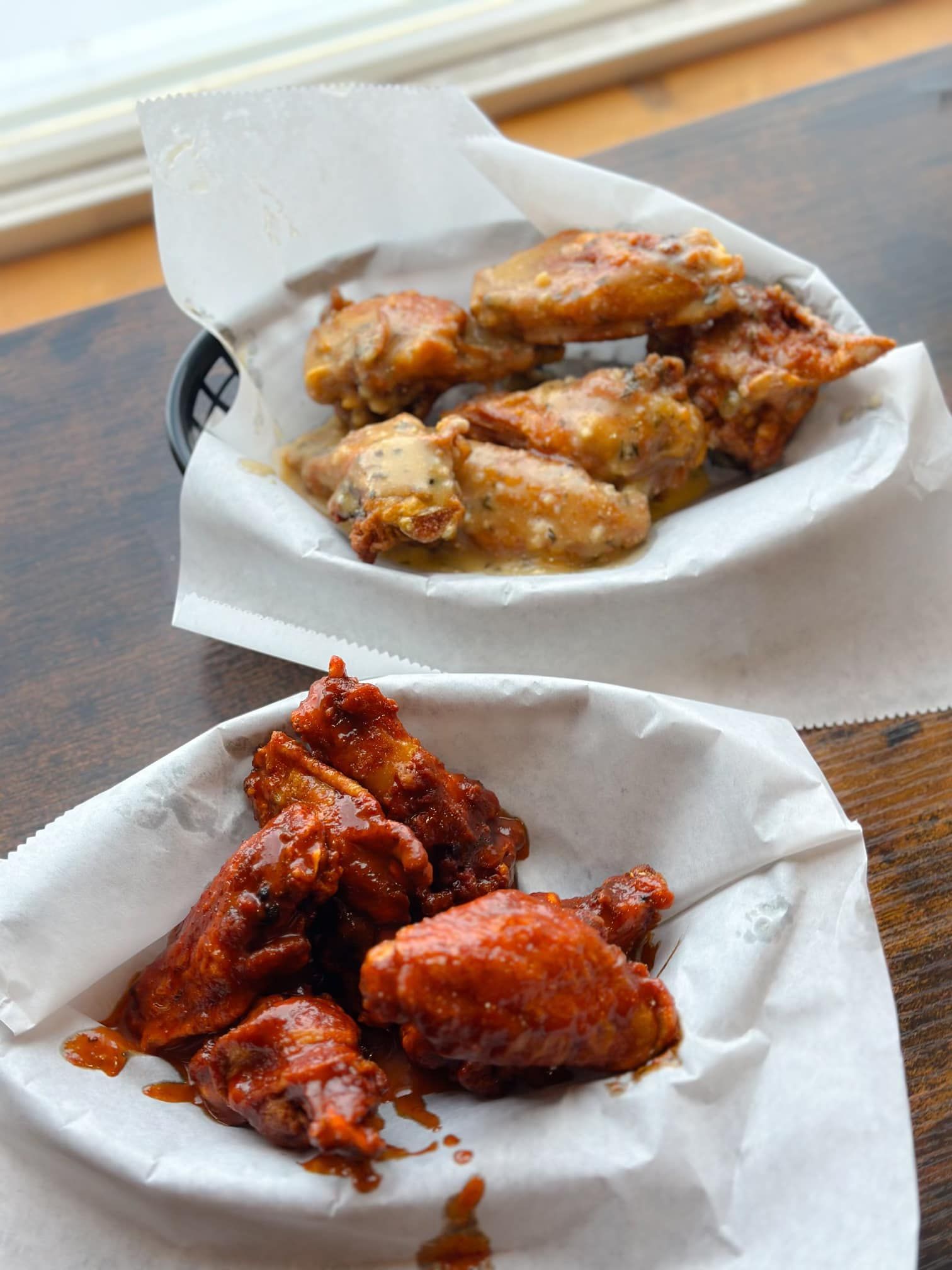 Two bowls of chicken wings are sitting on a wooden table.