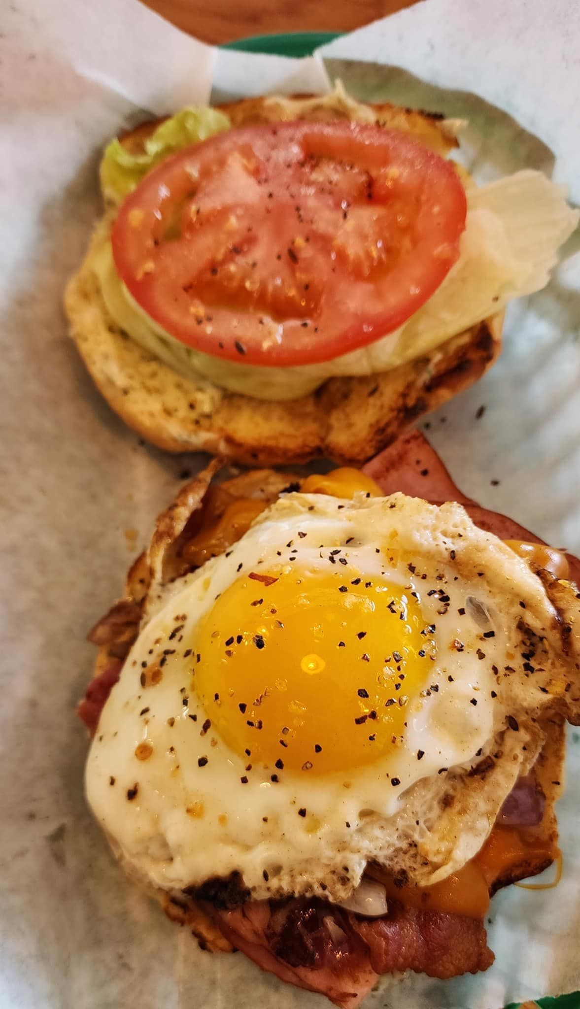A close up of a sandwich with eggs , bacon and tomatoes on a plate.