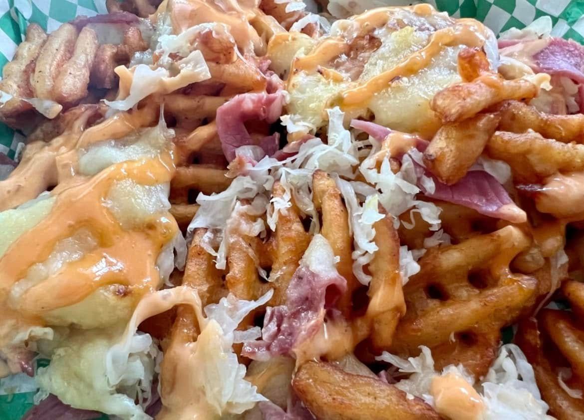 A close up of a green basket filled with french fries and cheese.