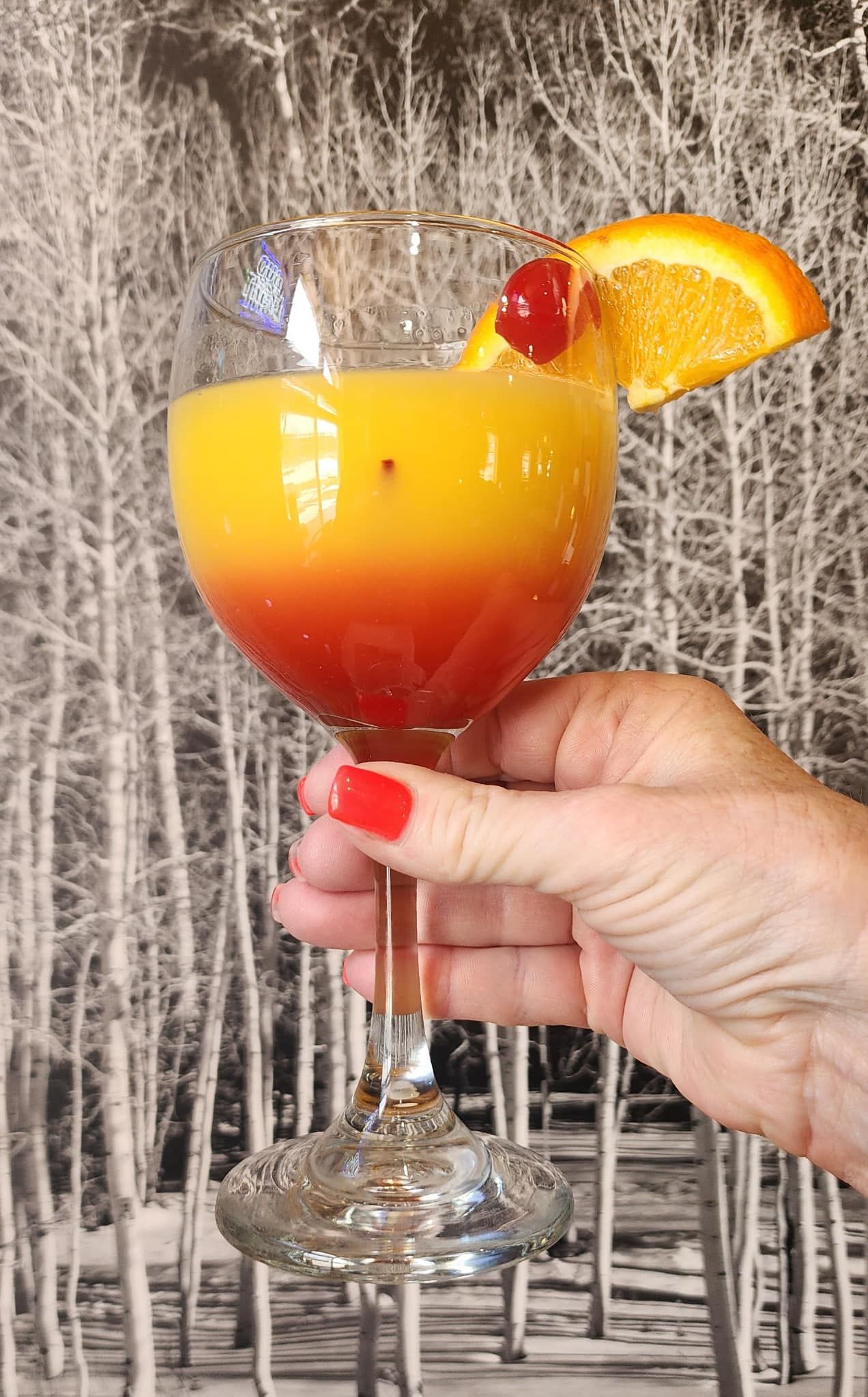 A person is holding a glass of orange juice with a cherry on top.