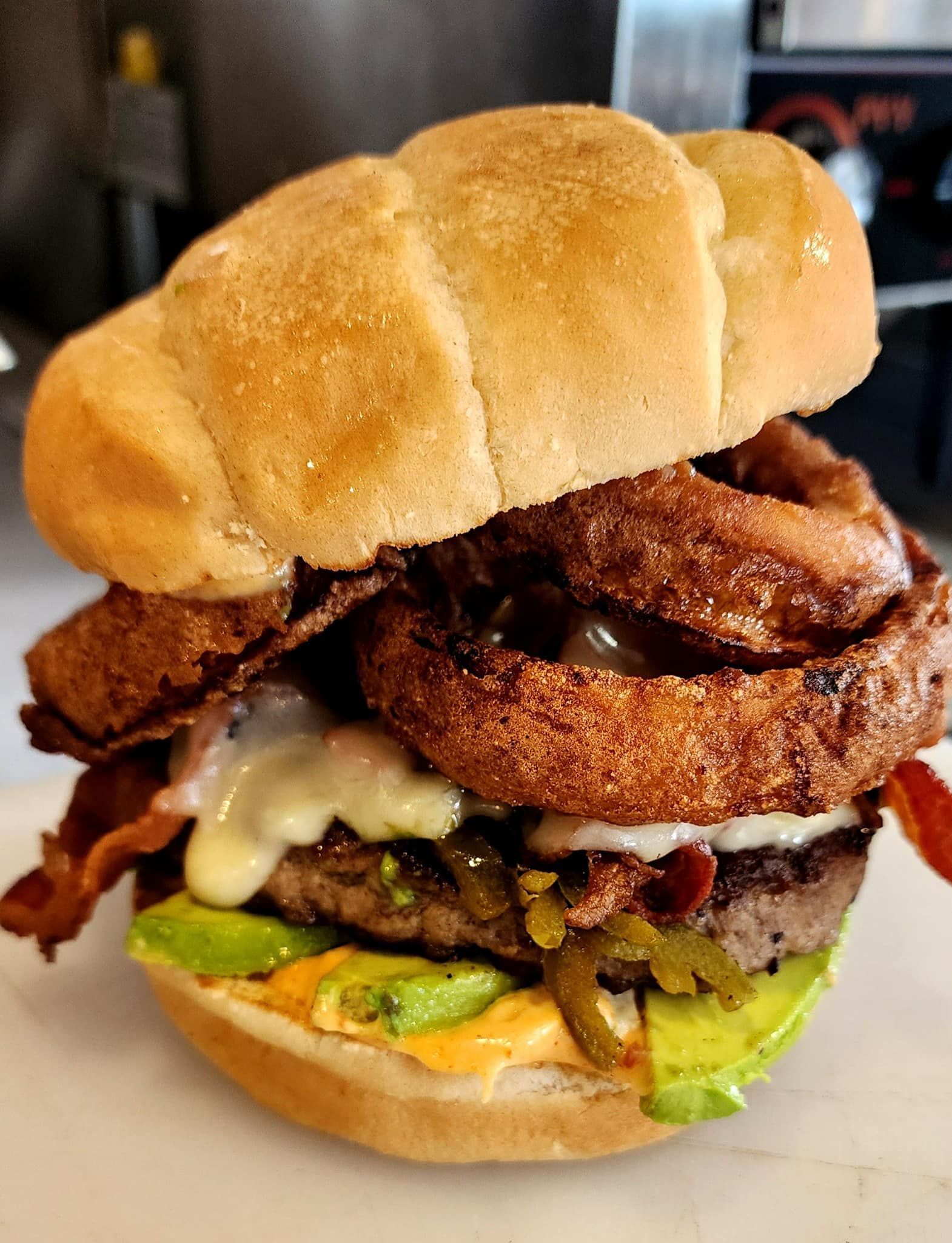 A close up of a hamburger with onion rings and bacon on a bun.