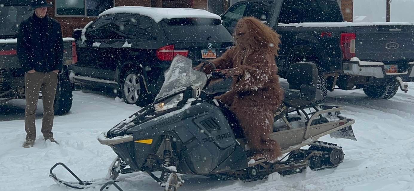 A man and a bear are riding a snowmobile in the snow.
