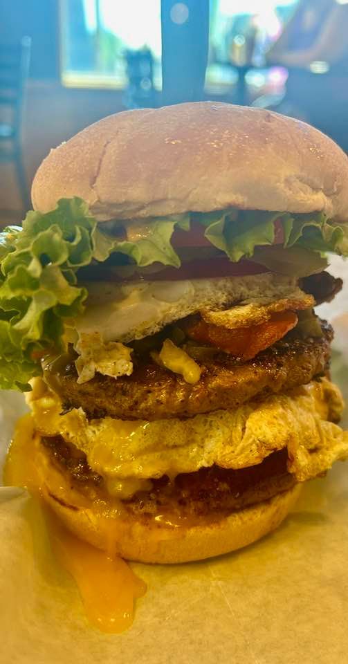 A close up of a hamburger with eggs , lettuce , tomatoes and cheese on a bun.