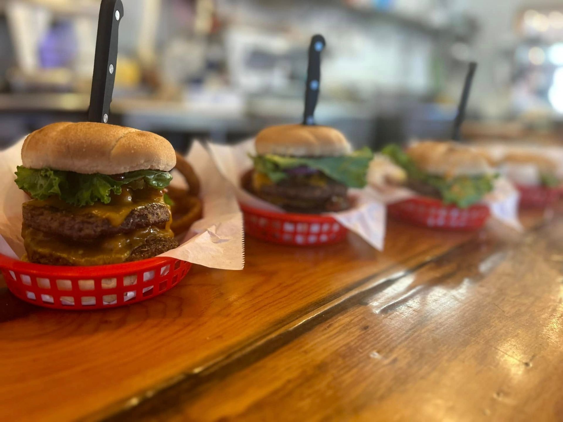 A row of hamburgers in red baskets on a wooden counter.