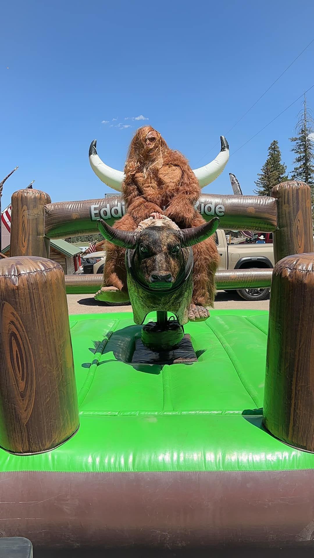 A bull is riding a mechanical bull on a green mat.