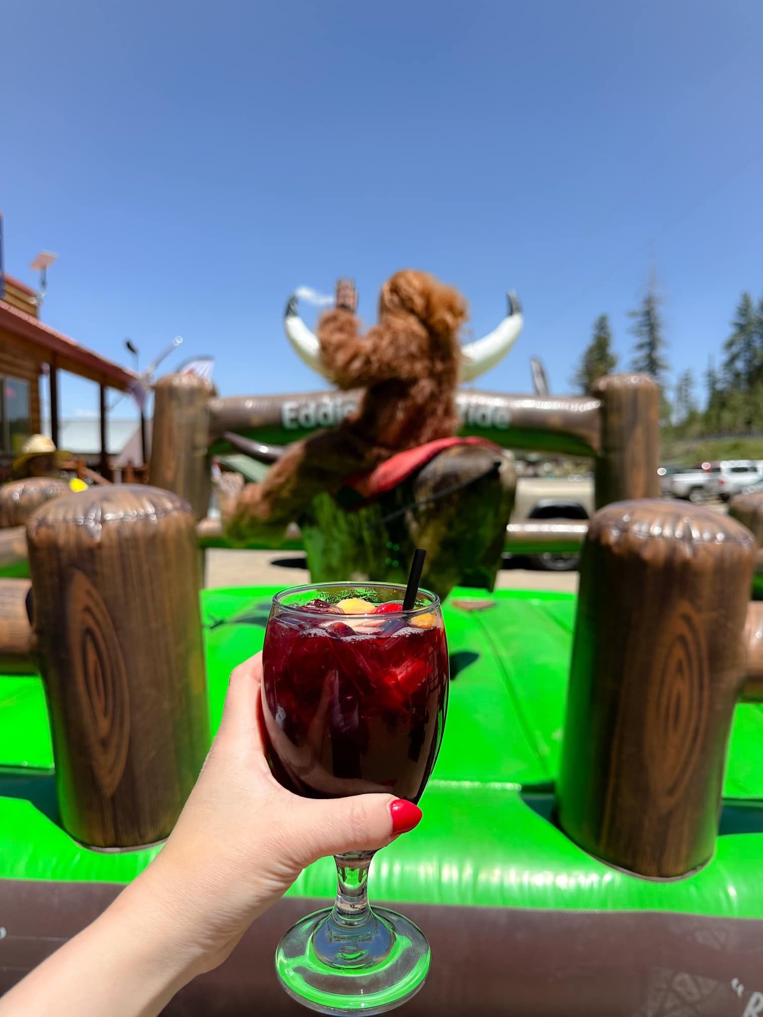 A person is holding a glass of wine in front of an inflatable bull.