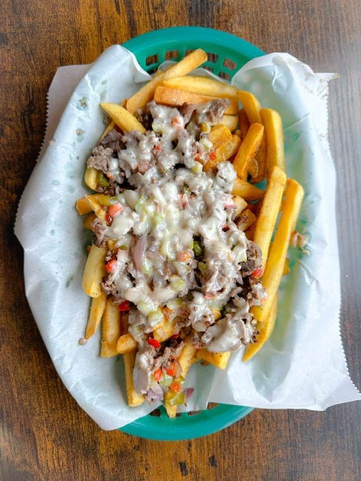 A basket of french fries with cheese and meat on a wooden table.