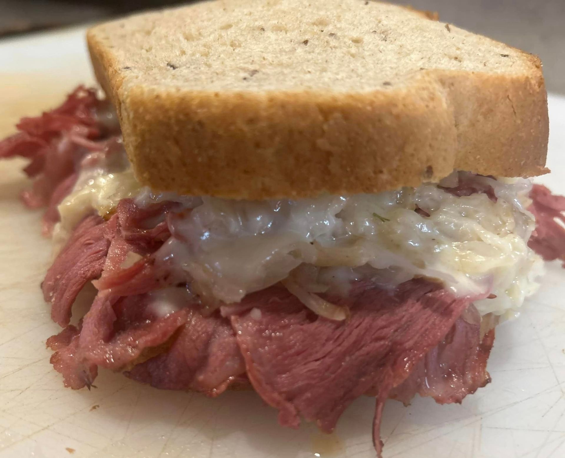 A close up of a corned beef sandwich on a piece of bread on a cutting board.