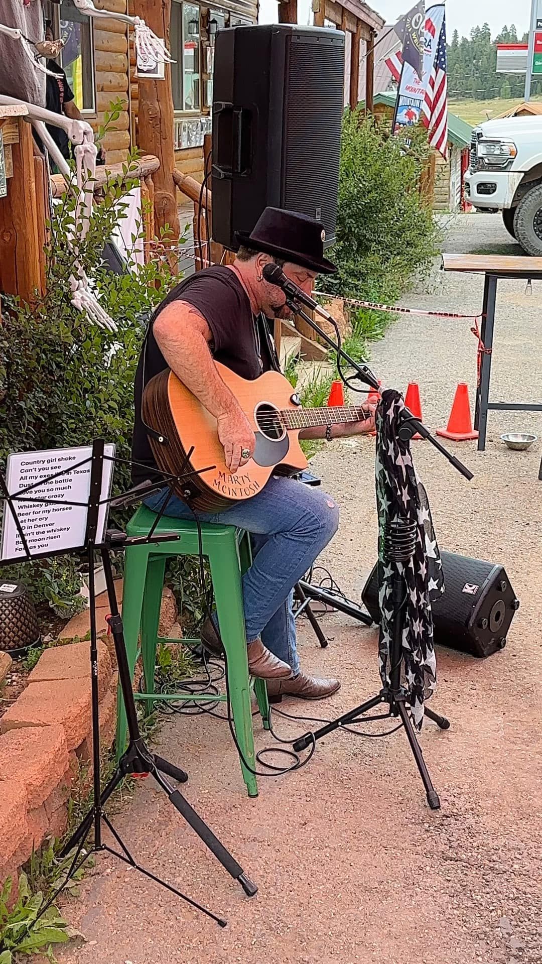 A man is sitting on a green stool playing a guitar and singing into a microphone.