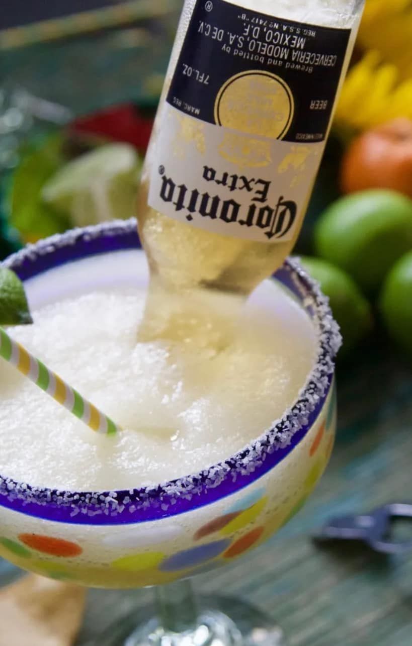 A bottle of corona extra is being poured into a margarita
