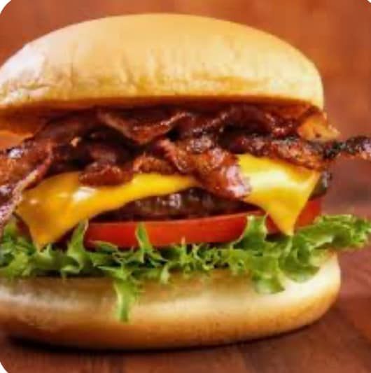 A hamburger with cheese , bacon , lettuce and tomato on a bun on a wooden table.