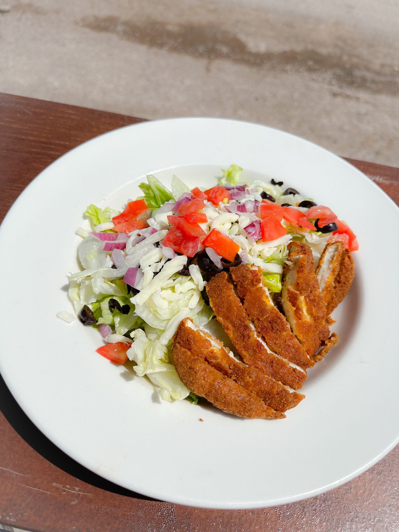 A white plate topped with a salad and chicken on a wooden table.