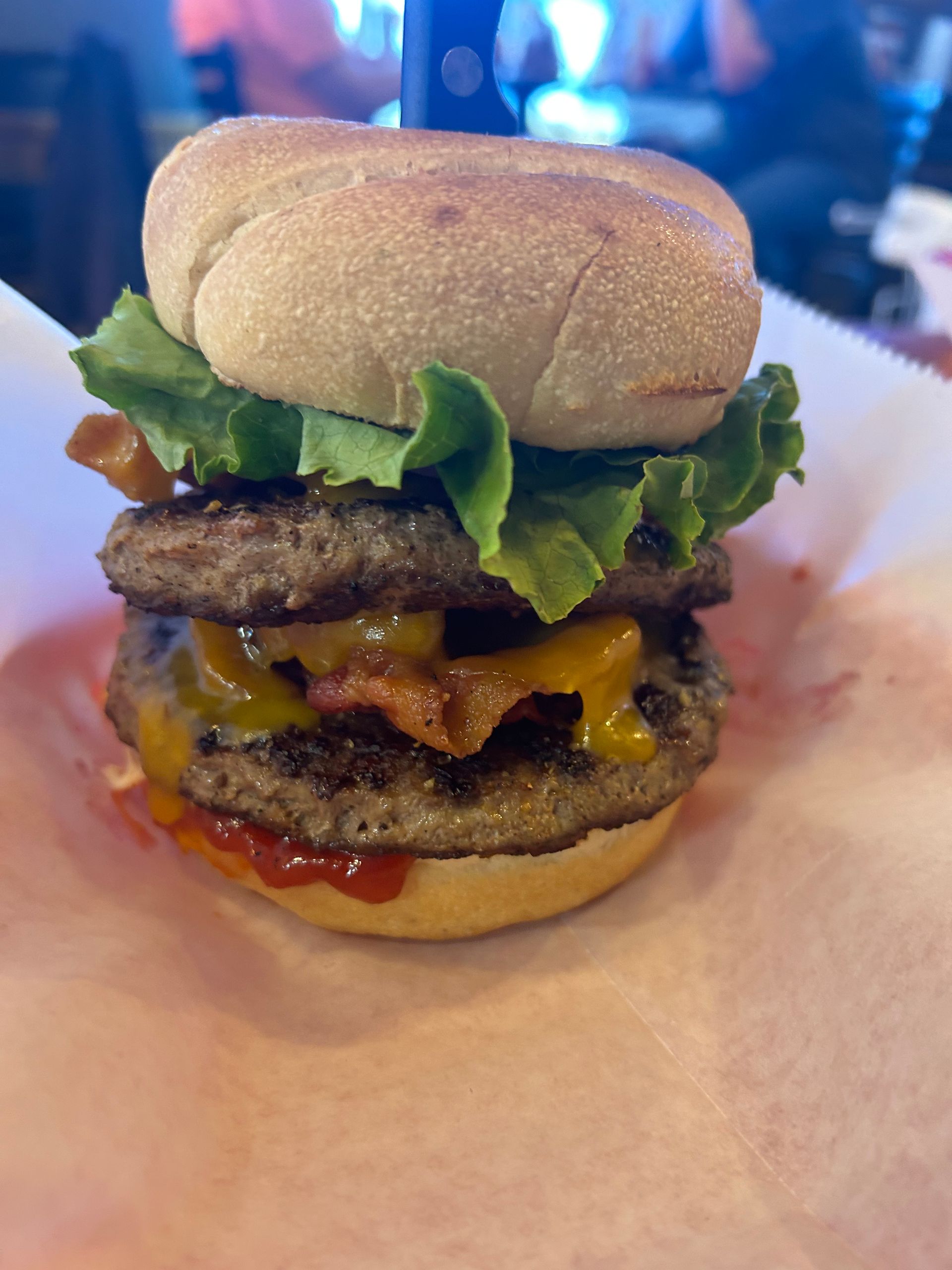 A double cheeseburger with lettuce , bacon and ketchup on a bun.