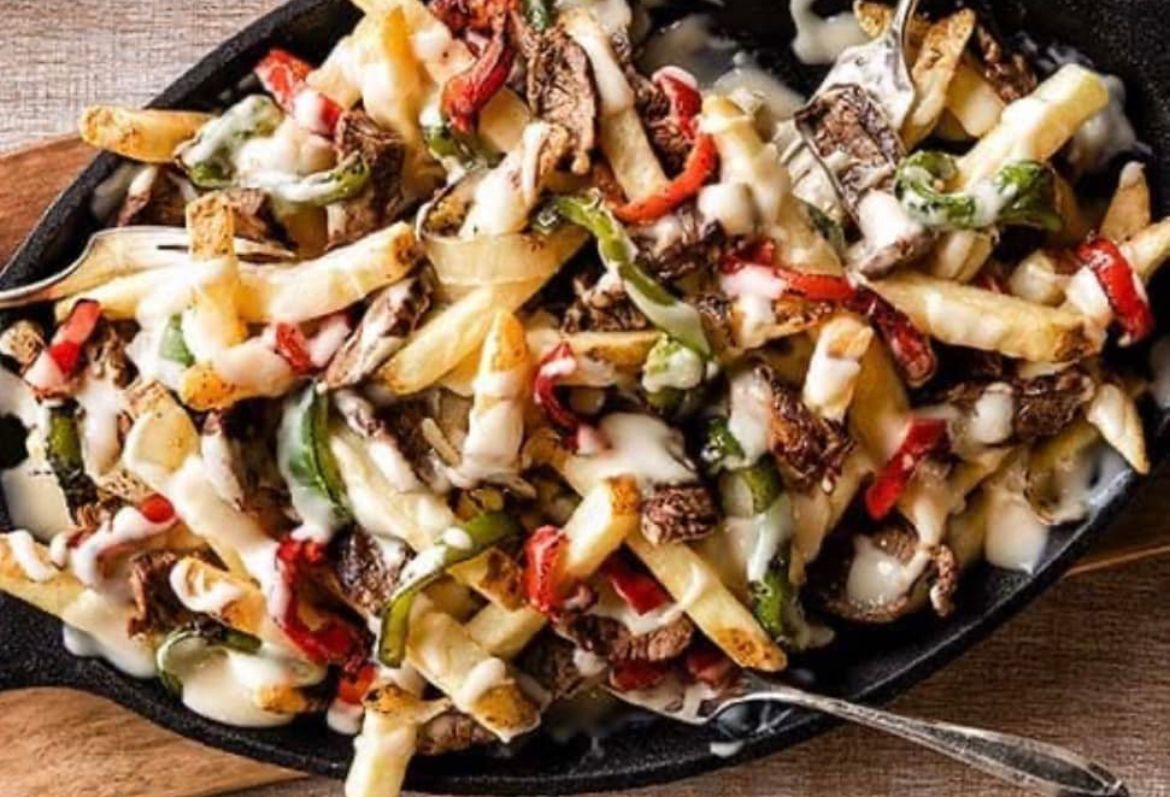 A skillet filled with french fries and vegetables with a spoon in it.