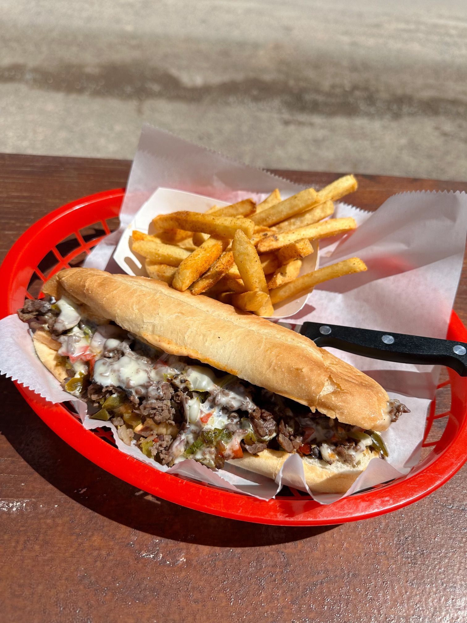 A sub sandwich and french fries in a red basket on a table.