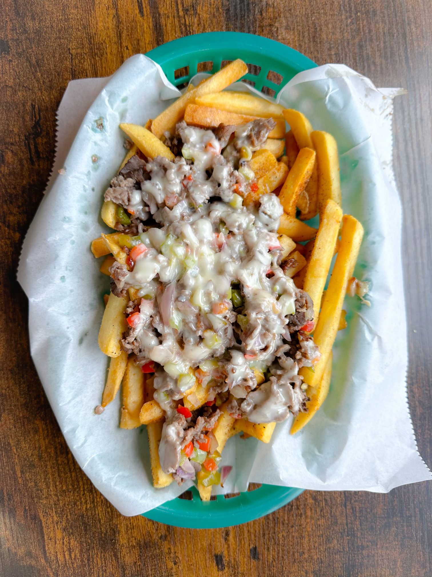 A basket of french fries with cheese and meat on a wooden table.