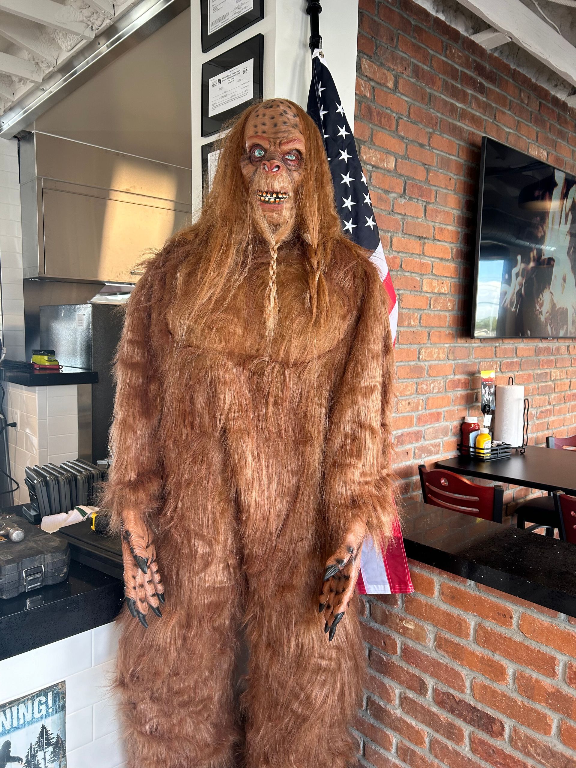 A bigfoot statue is standing in front of a brick wall in a restaurant.