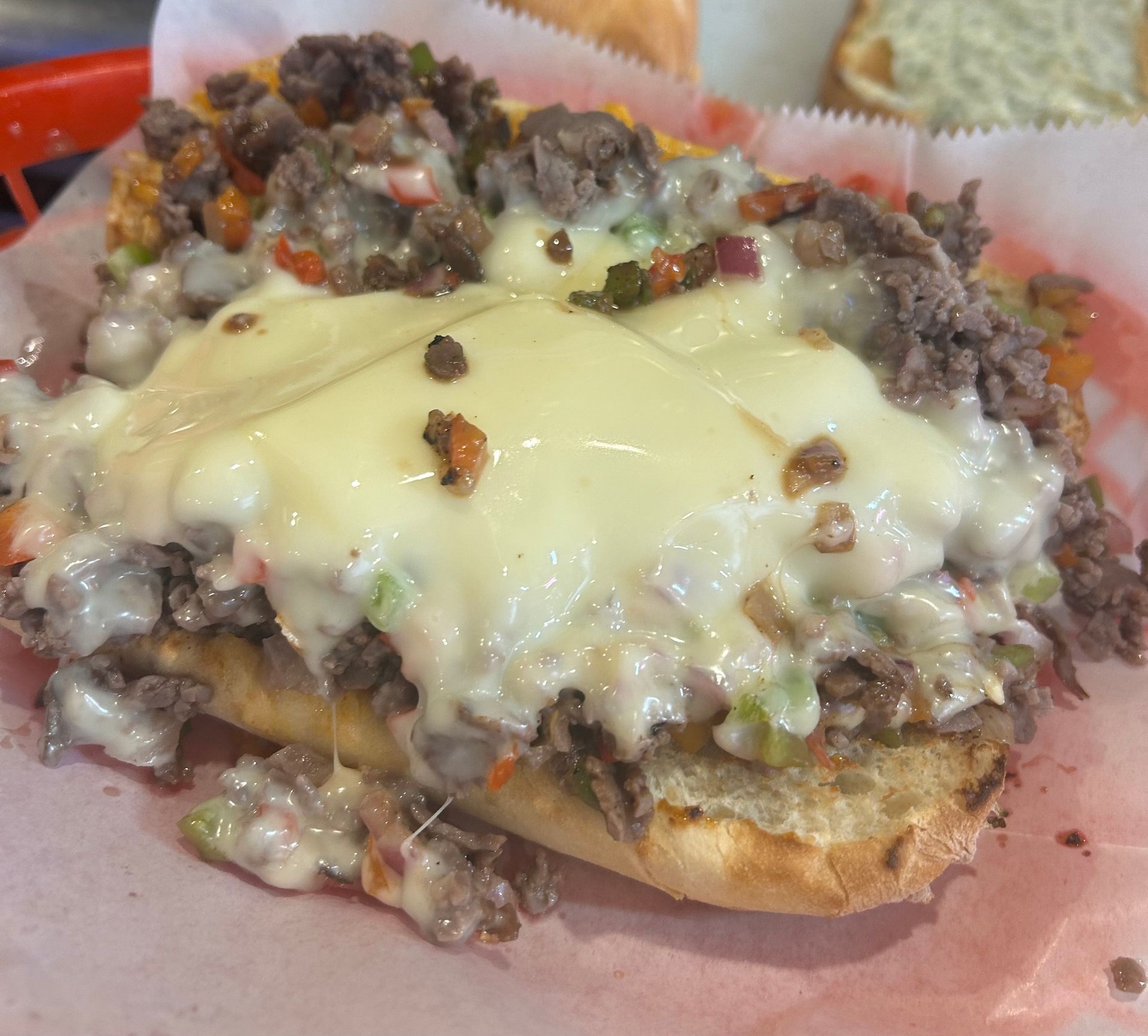 A close up of a steak sandwich with cheese on a bun on a table.