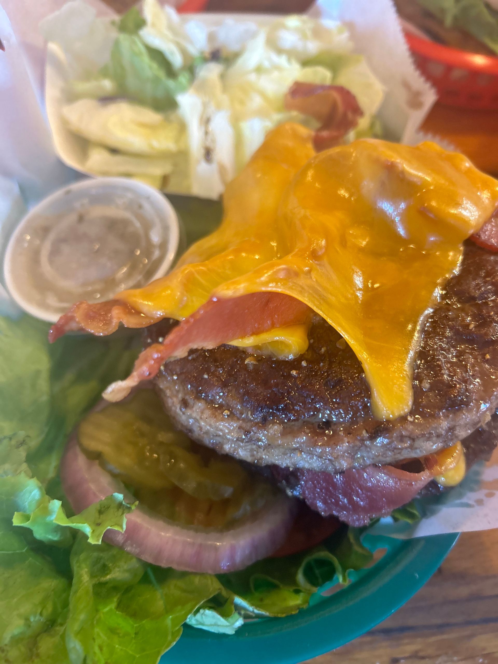 A close up of a hamburger with cheese , bacon and lettuce on a plate.