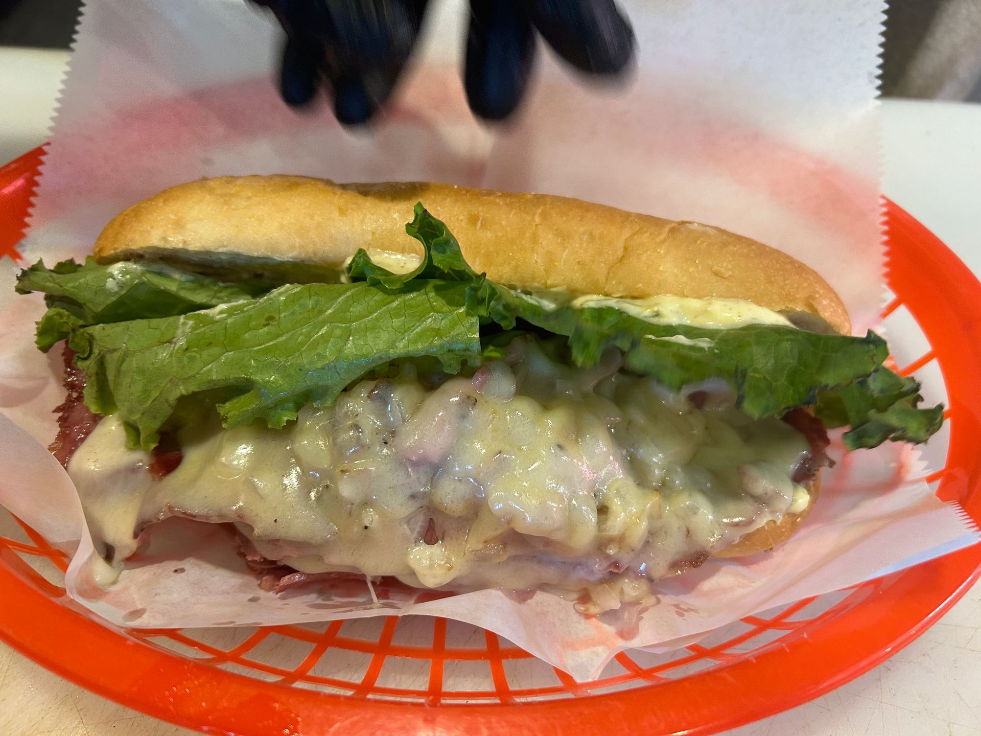 A sub sandwich with lettuce and cheese on a bun in an orange basket.