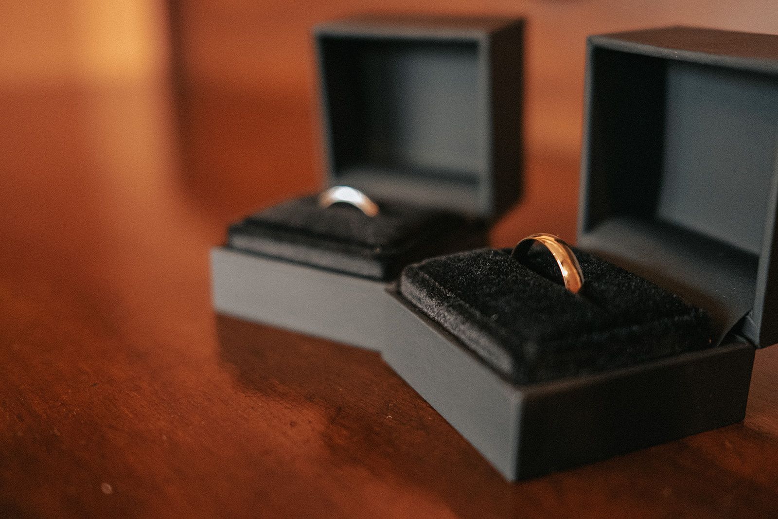 Two wedding rings are in black boxes on a wooden table.