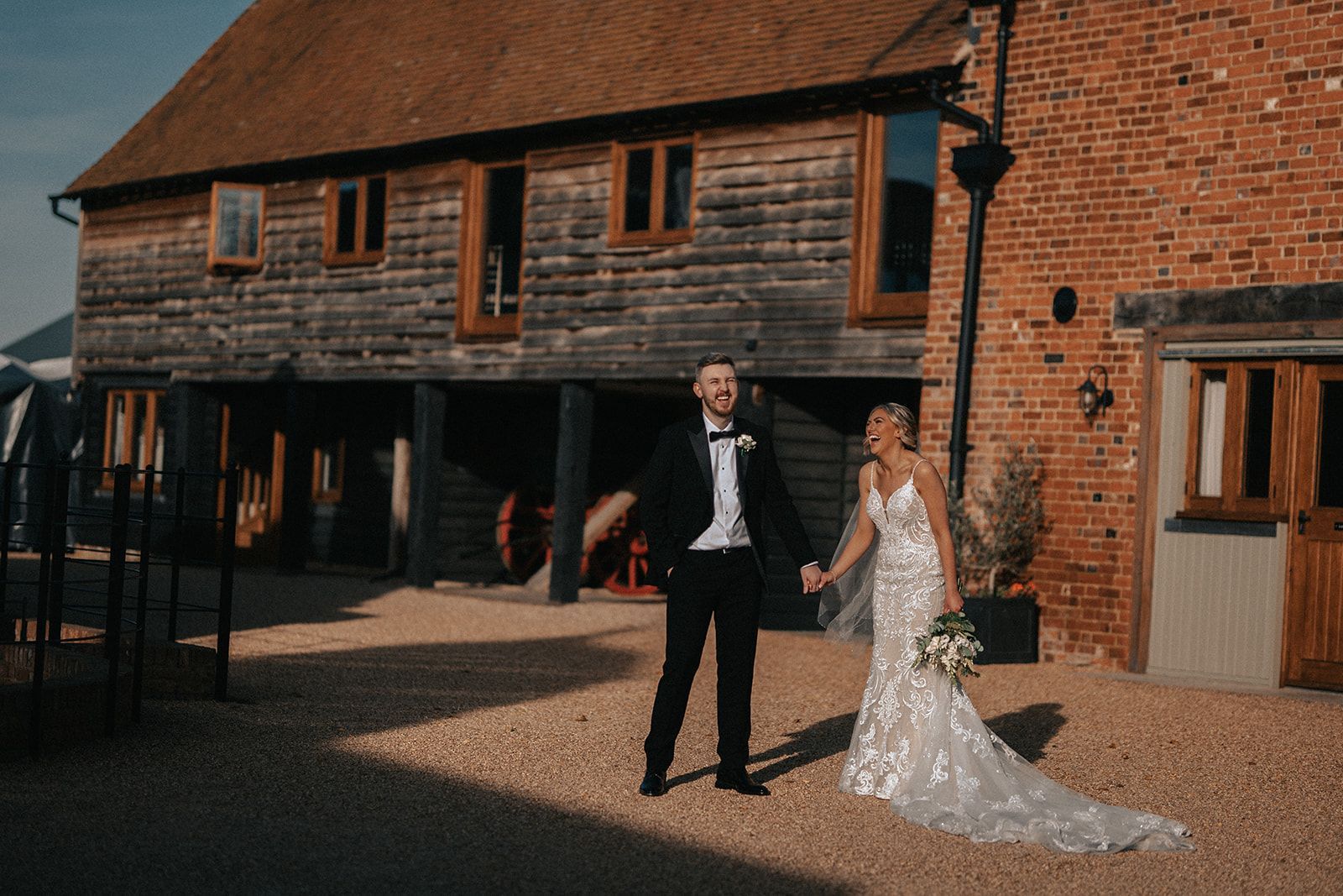 A bride and groom are standing in front of a brick building holding hands.