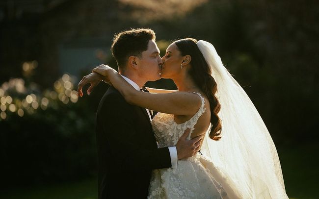 A bride and groom are walking in a field holding hands.