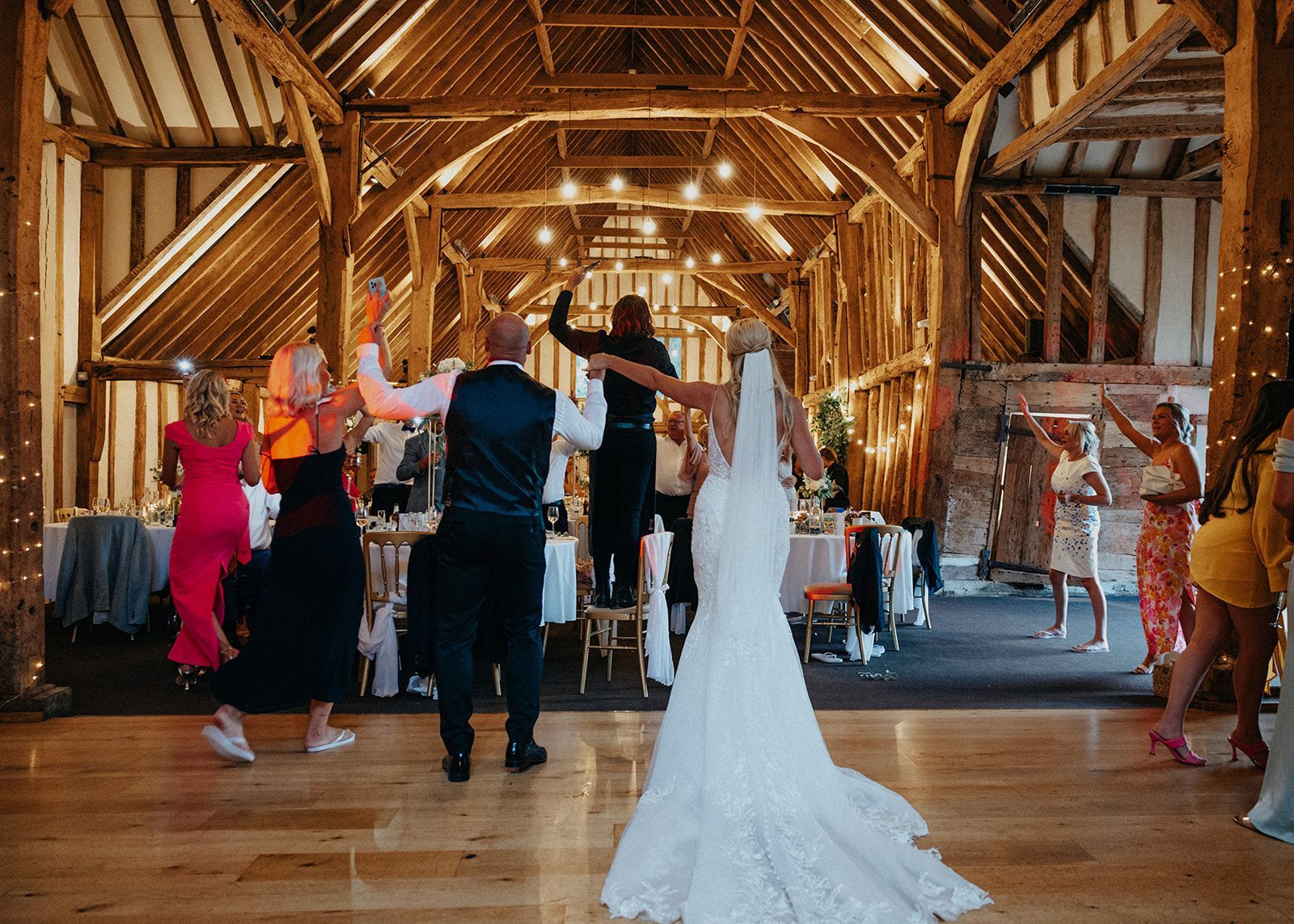A bride and groom are dancing with their wedding guests in a barn.