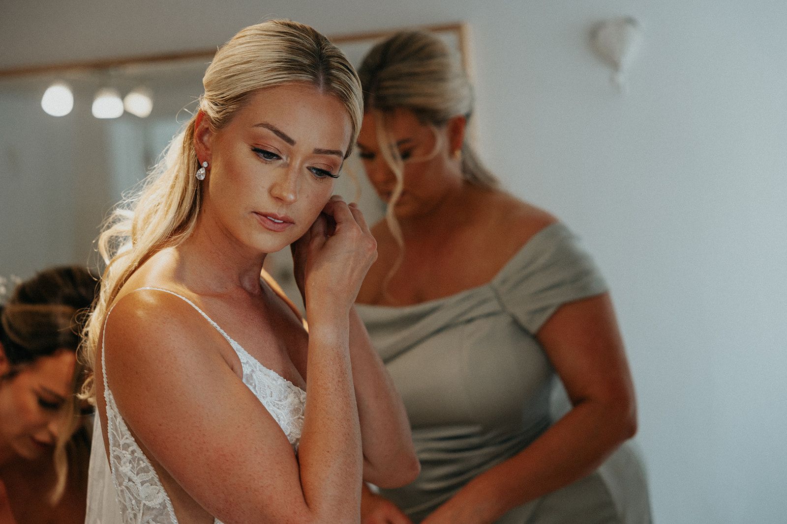 A woman in a wedding dress is putting on her earrings.