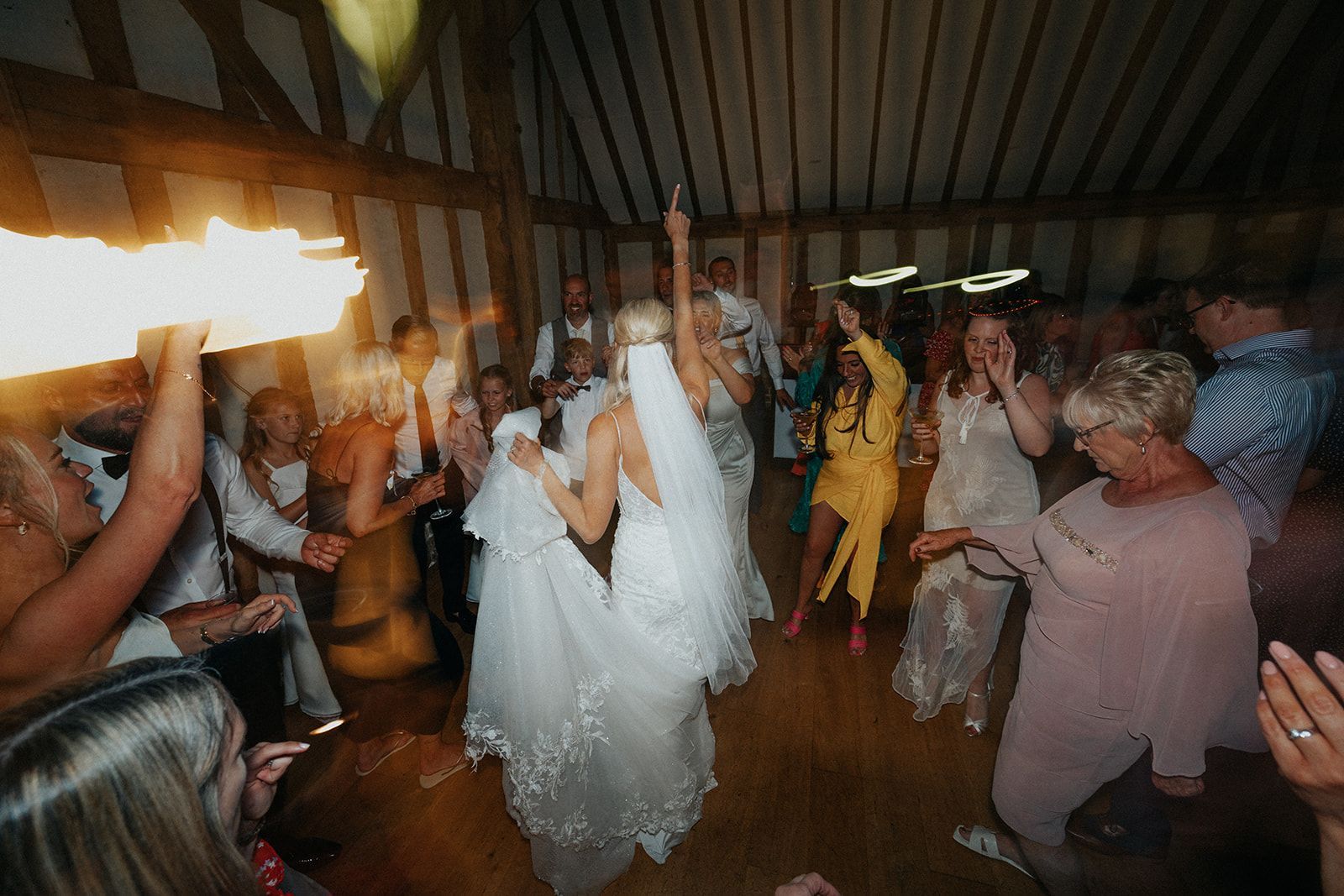 A group of people are dancing at a wedding reception in a barn.