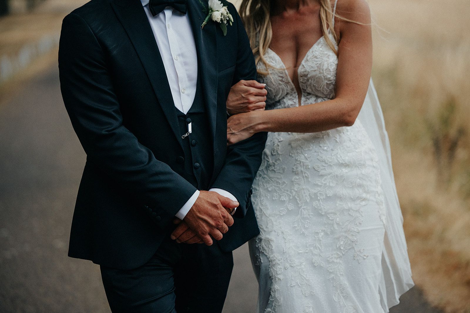 A bride and groom are walking down a road holding hands.