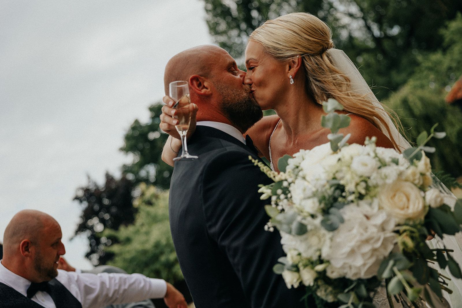 A bride and groom kissing while holding a glass of champagne.