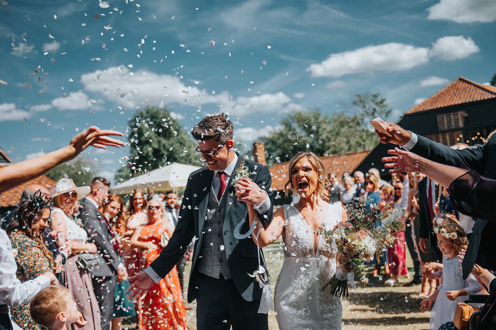 A bride and groom are walking through a crowd of people throwing confetti at them.