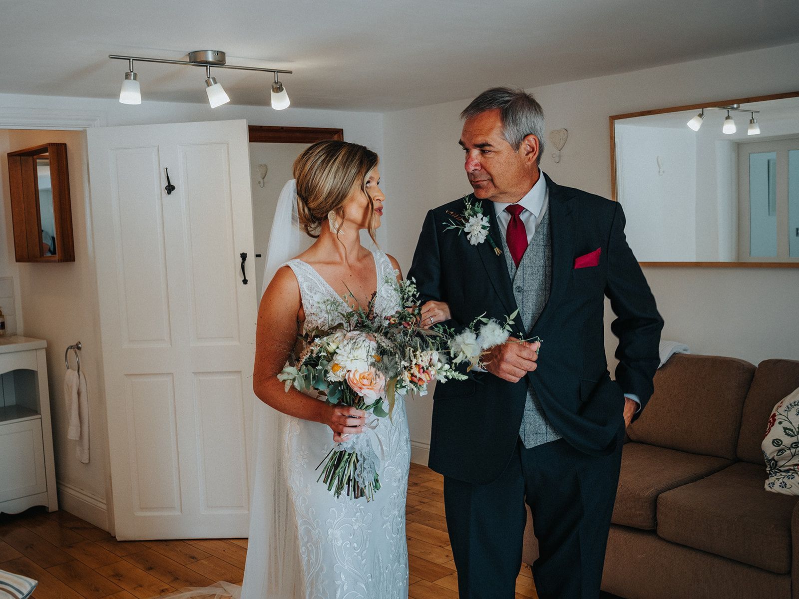 A bride and her father are standing next to each other in a living room.