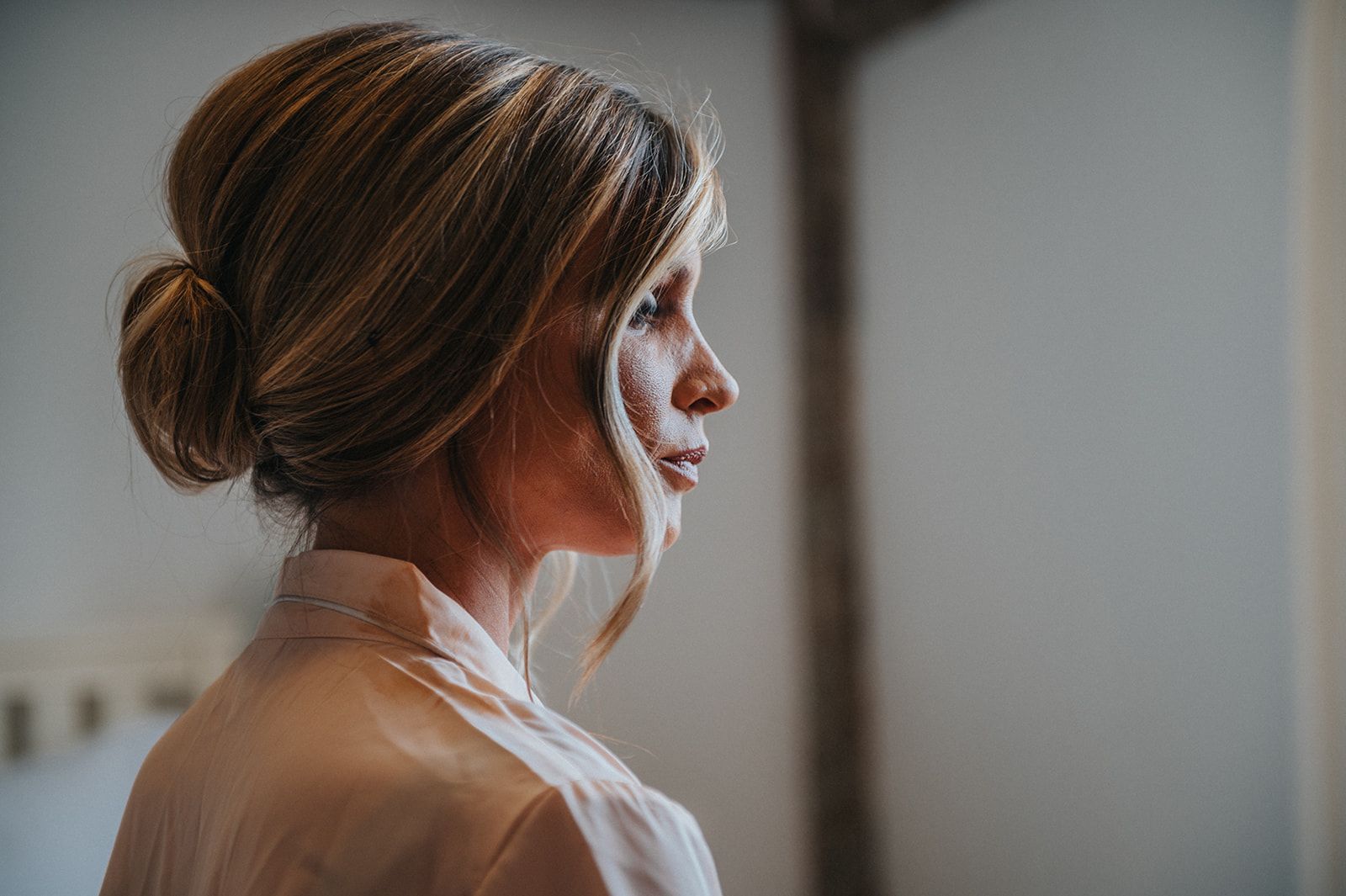 A woman with her hair in a bun is standing in front of a window.