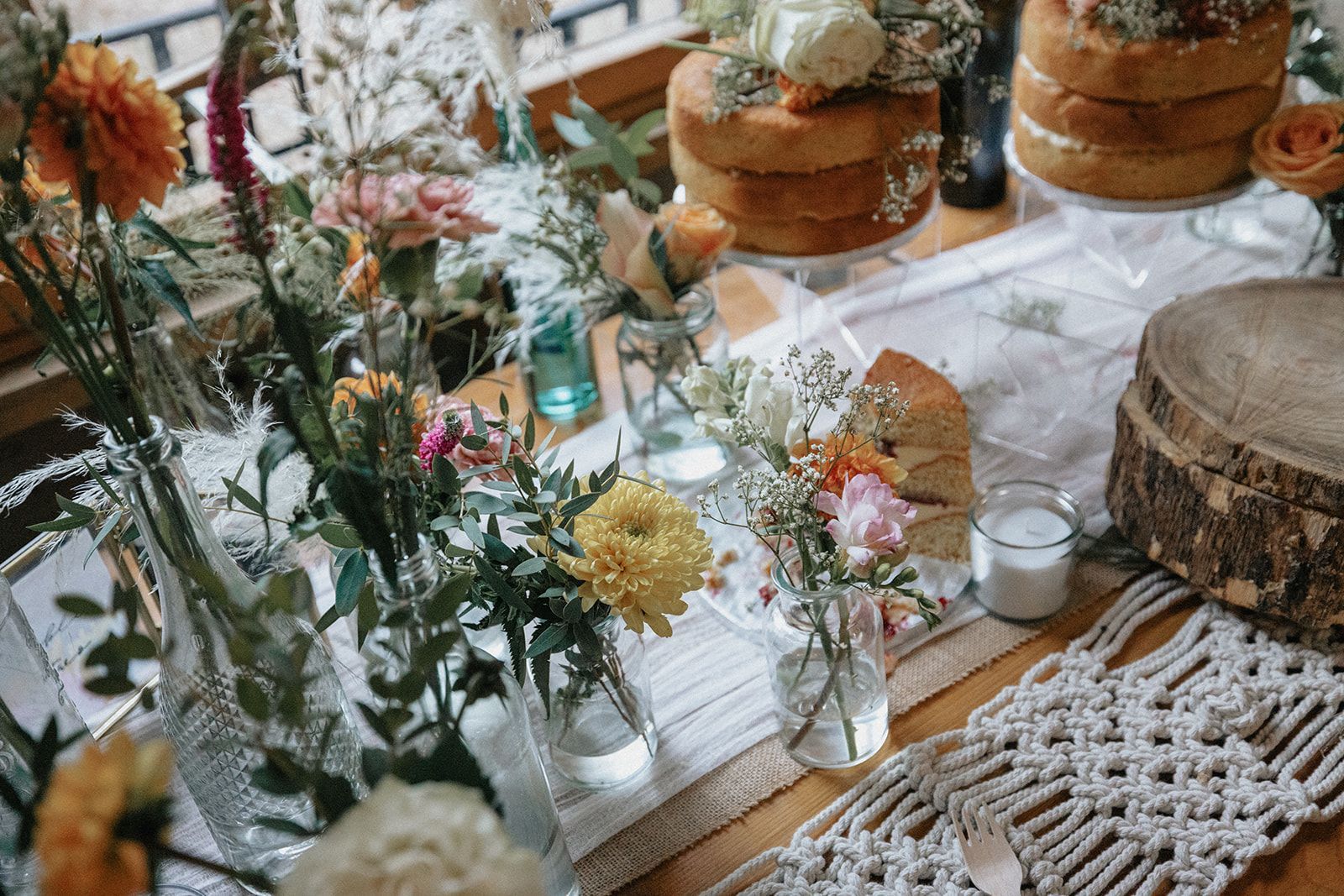 A table topped with vases of flowers and cakes.