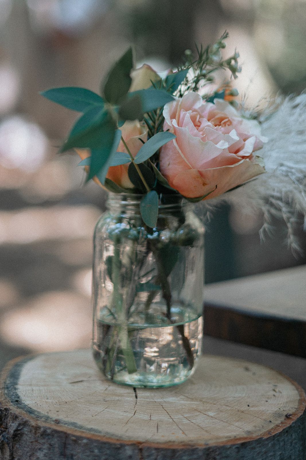A mason jar filled with water and flowers is sitting on a wooden stump.