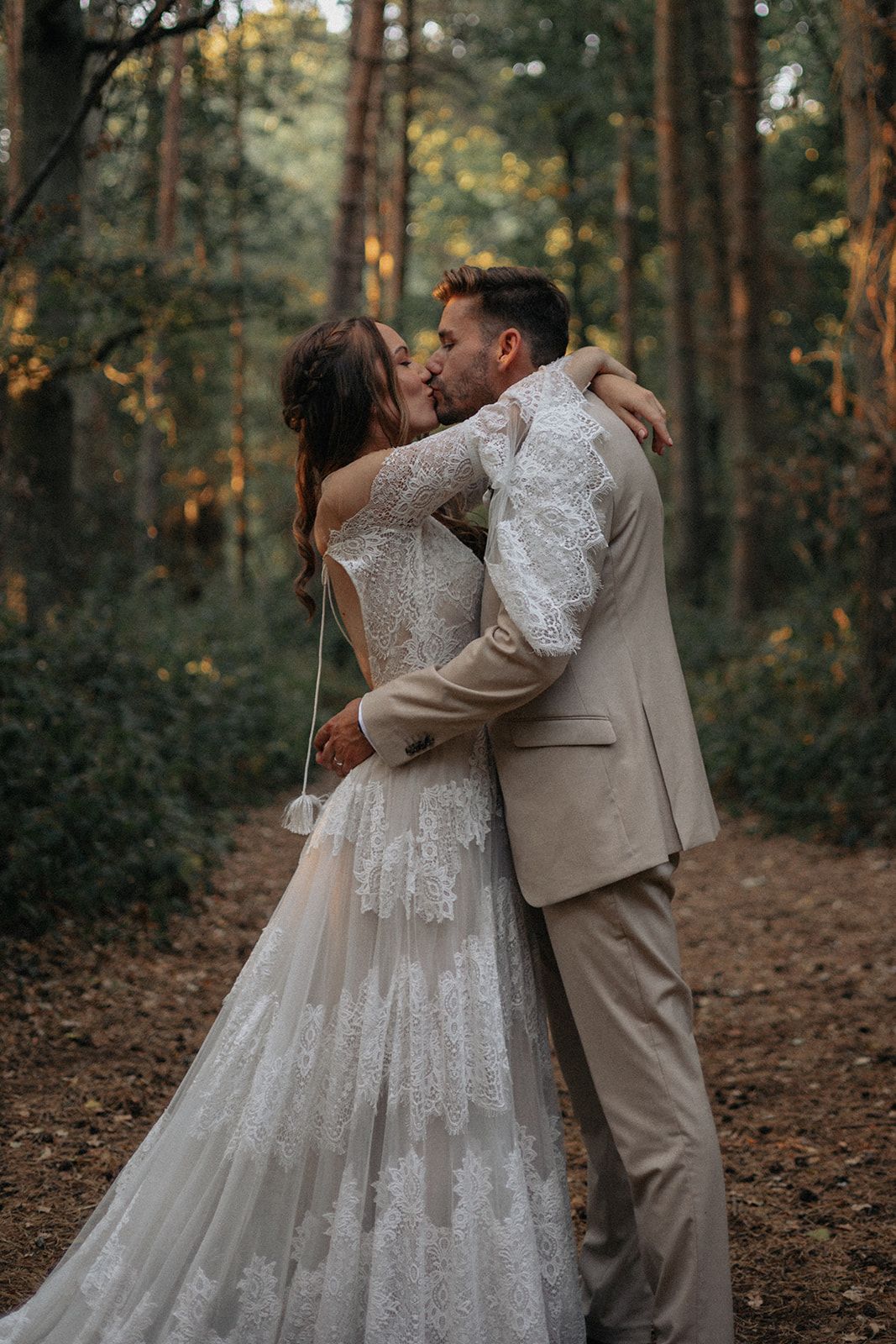 A bride and groom are kissing in the woods.