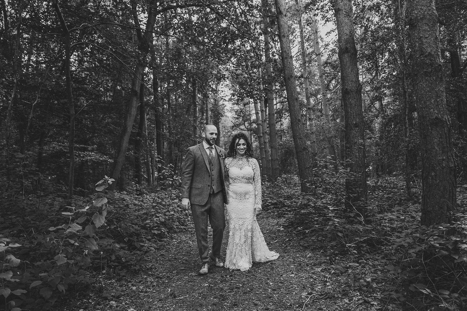 A bride and groom are walking through a field holding hands.
