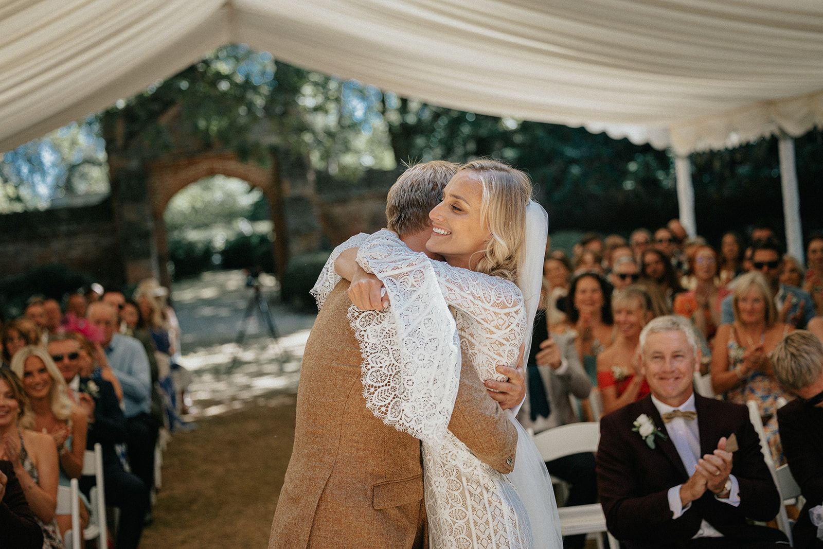 A bride and groom are hugging each other during their wedding ceremony under a tent.