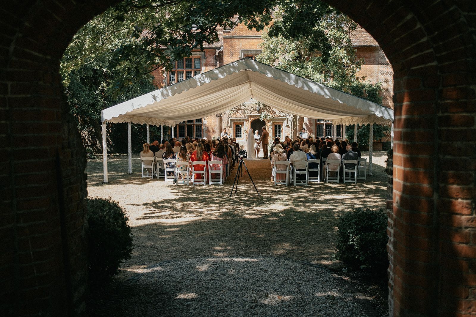 A group of people are sitting under a tent at a wedding ceremony.