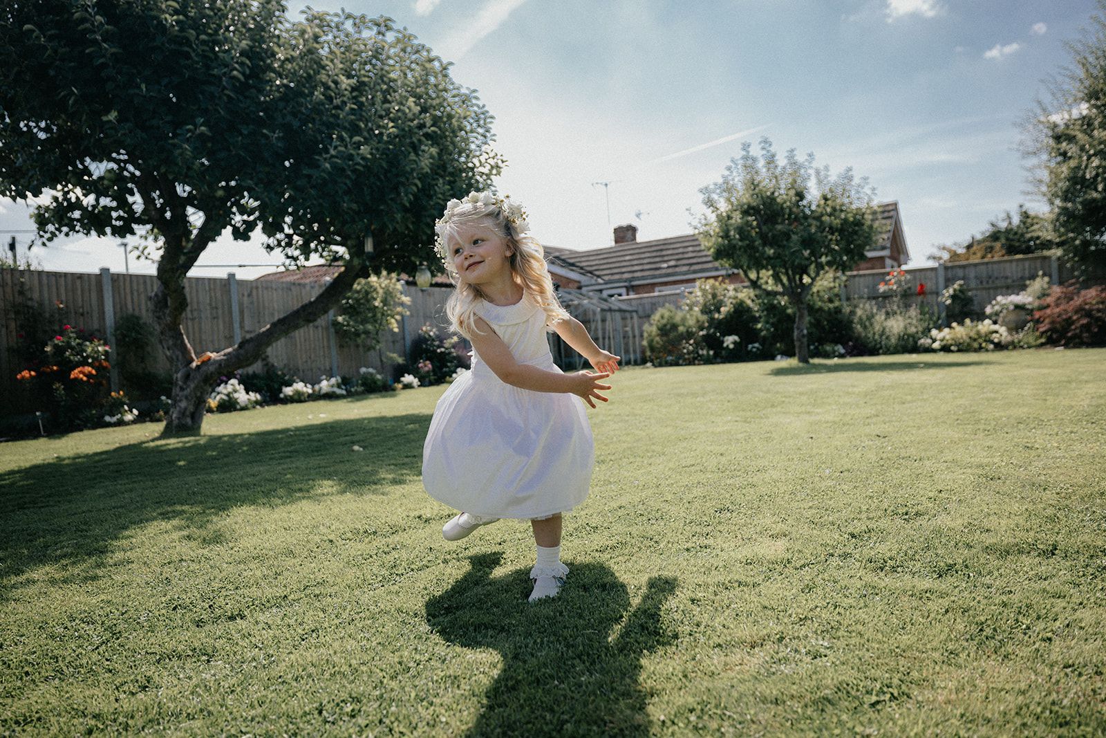 A little girl in a white dress is standing on a lush green lawn.
