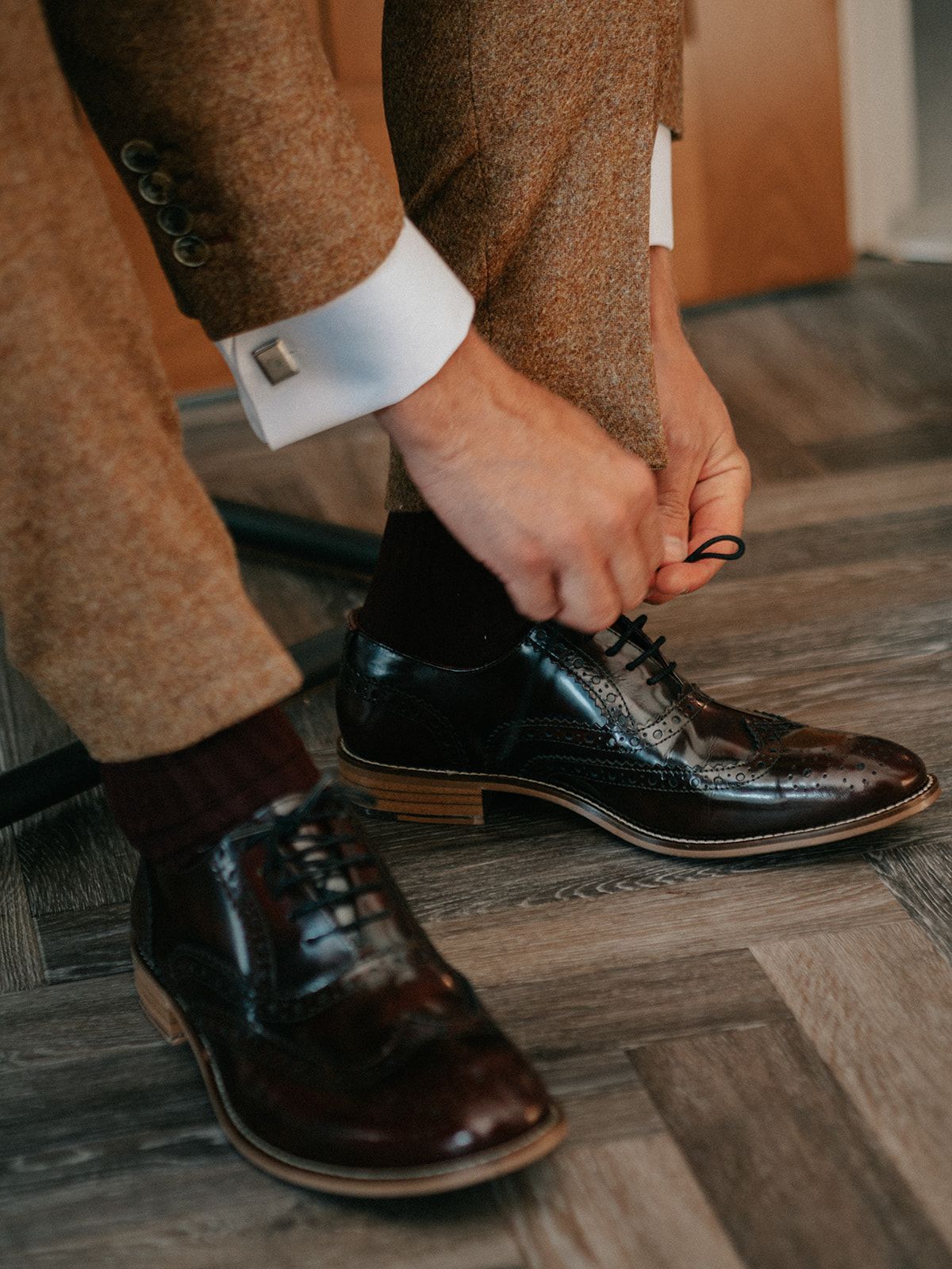 A man is tying his shoes on a wooden floor.