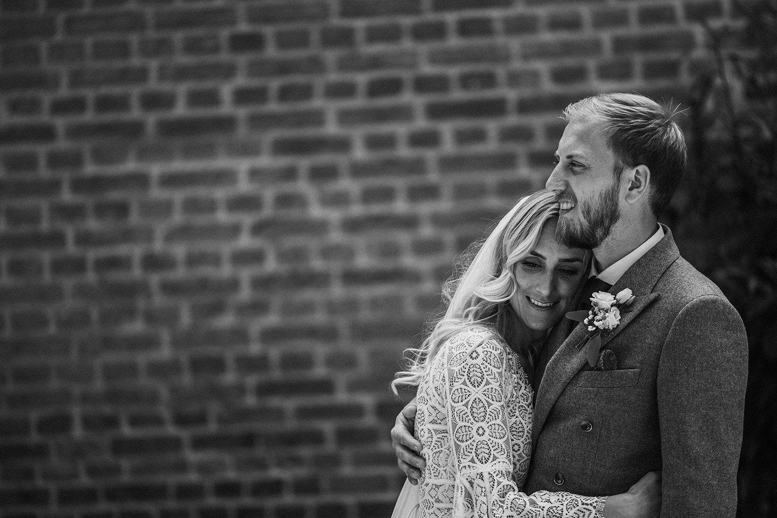 A black and white photo of a bride and groom hugging in front of a brick wall.