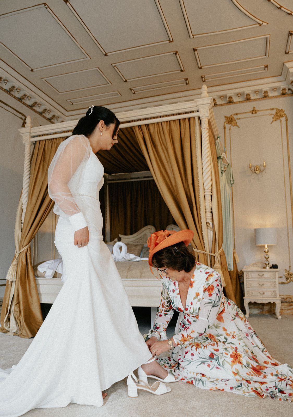 A woman is helping a bride put on her wedding shoes.