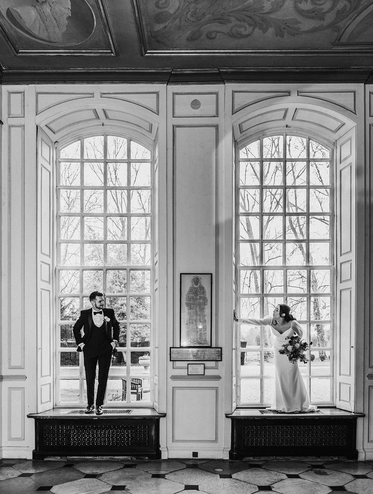A black and white photo of a bride and groom standing in front of a window