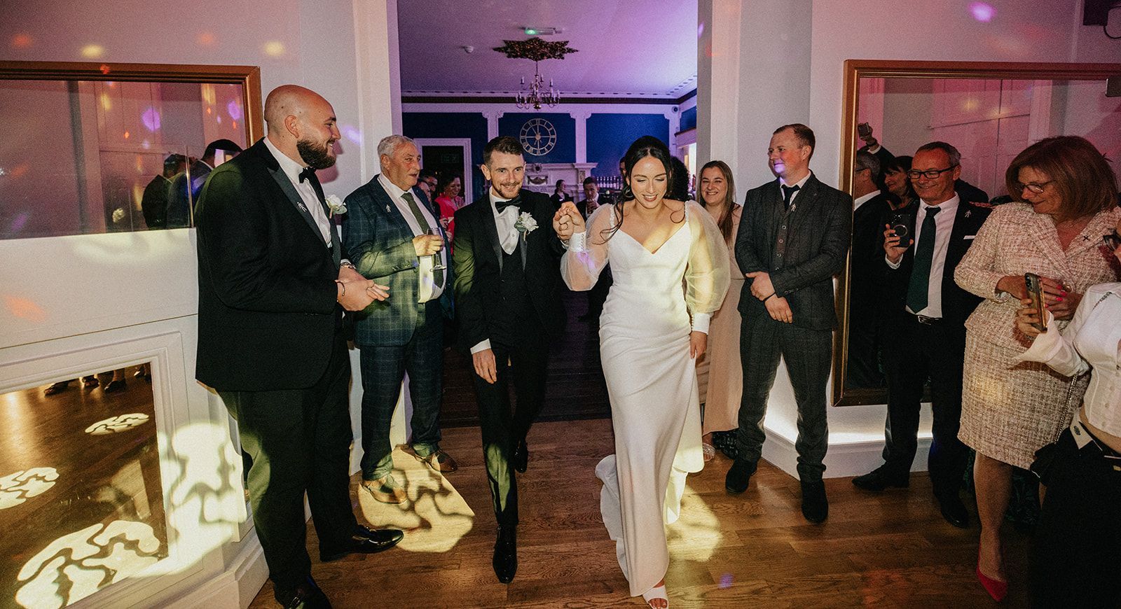 A bride and groom are walking through a crowd of people at a wedding reception.