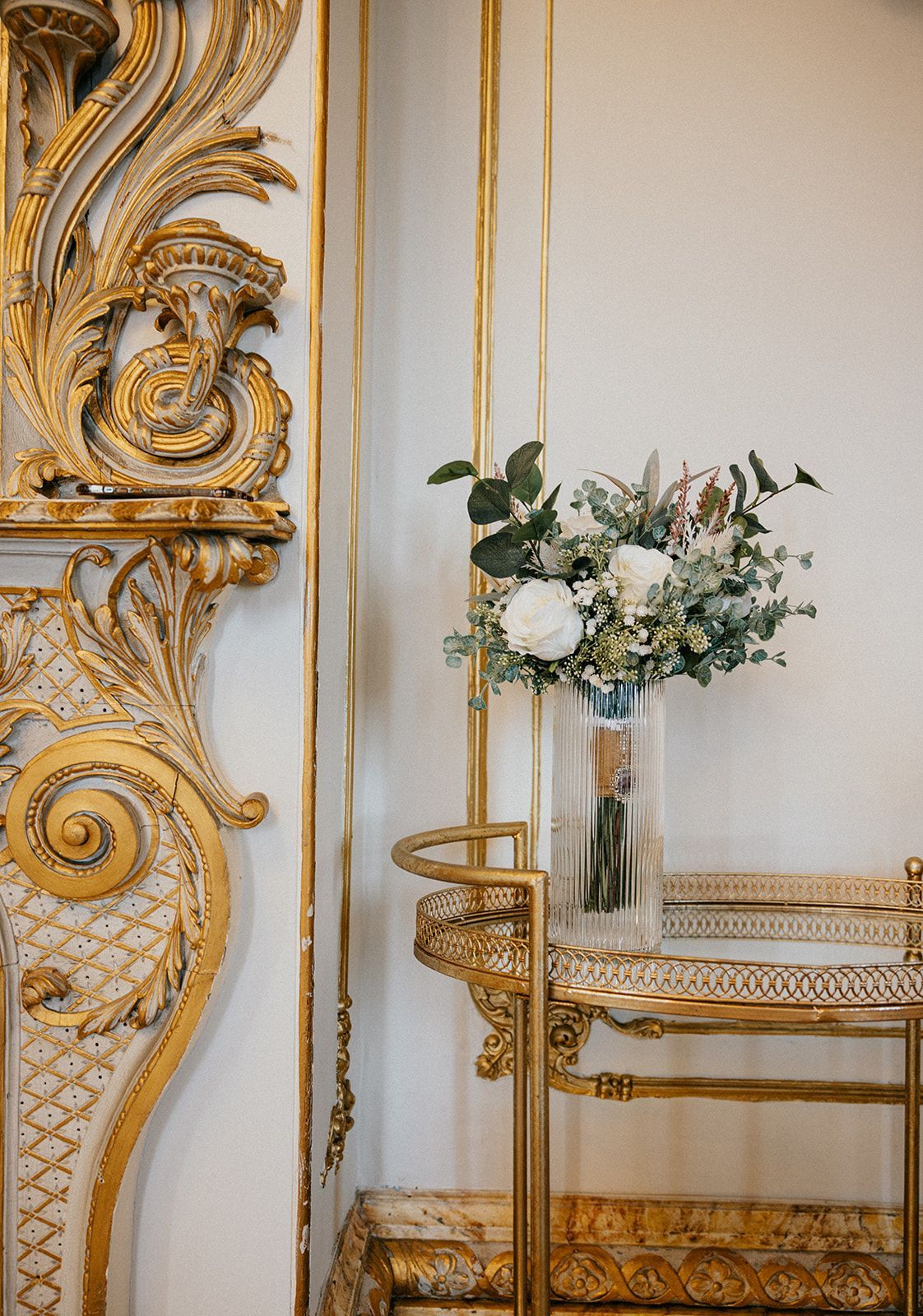 A vase of flowers is sitting on top of a gold bar cart.